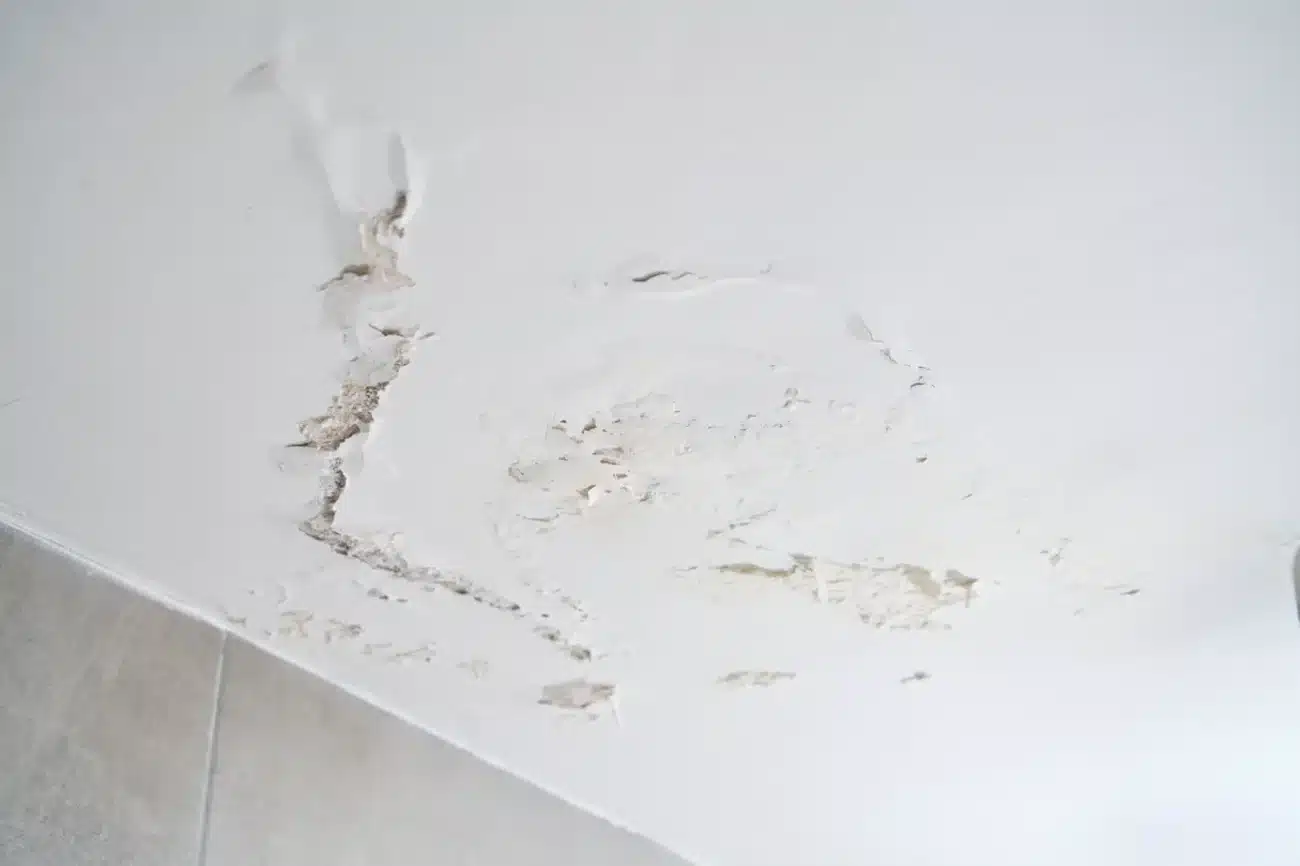 Poškodený strop s odlupujúcou sa omietkou a prasklinami spôsobenými vlhkosťou v interiéri domu